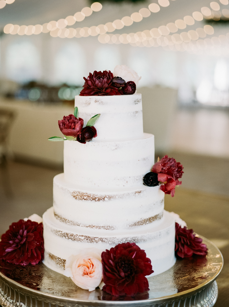 The wedding cake is decorated with burgundy and blush florals. 