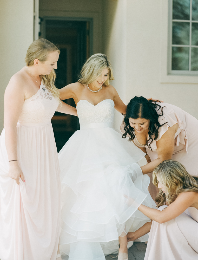 Bridesmaids help bride into her wedding shoes.