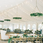 The white reception tent is brightly lit and decorated with lush greenery and colorful flowers at the Trail Creek Cabin wedding.