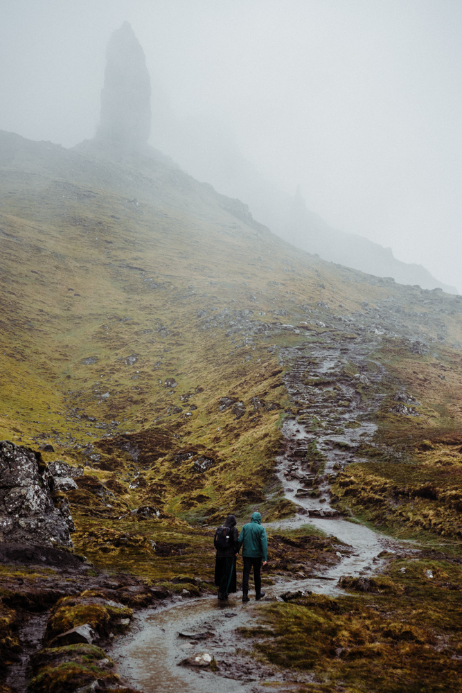 A couple walk together up a misty, wet path in the Isle of Skye.