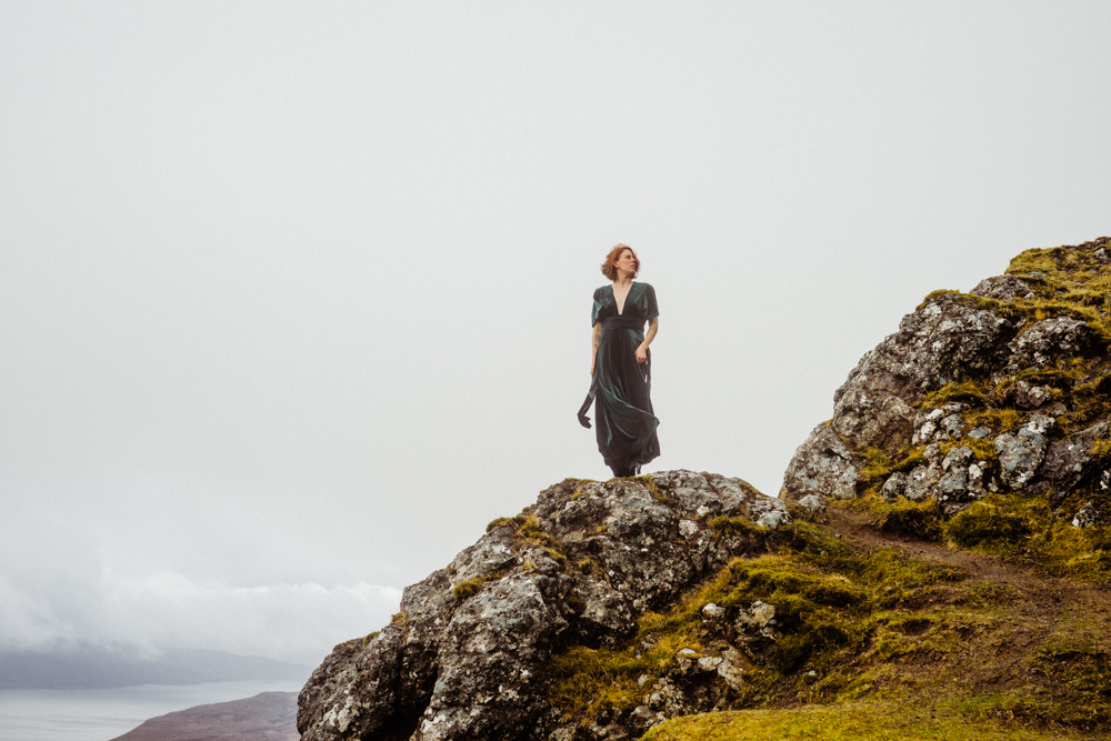A bride poses on a rocky outcrop in a green dress during her Isle of Skye elopement.