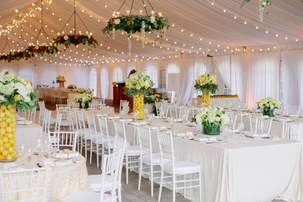 A wedding reception decorated with lemons and flowers in tall, clear vases.